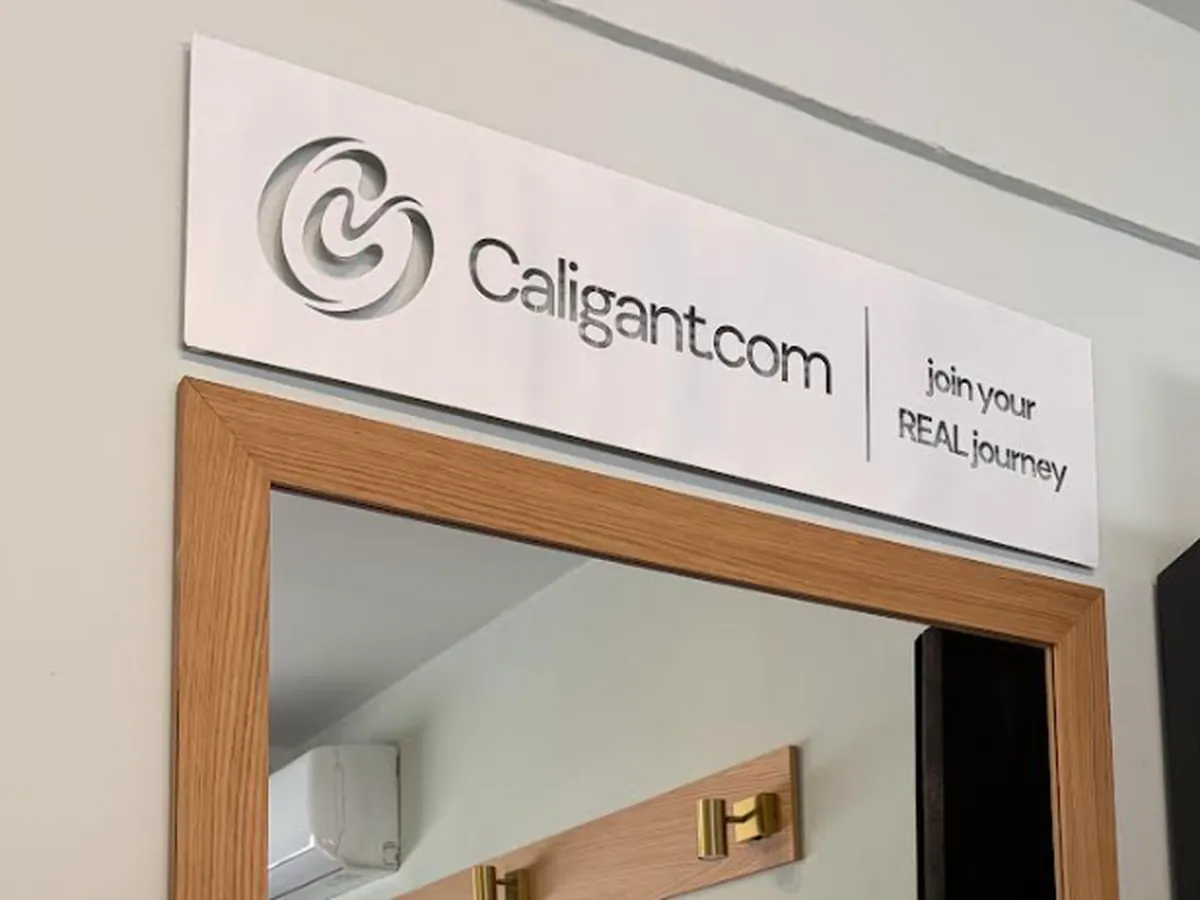 White Caligant sign with the cut-out symbol, Caligant.com and the tagline join your REAL journey, mounted above a wooden door frame
