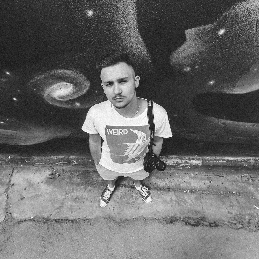 Nebojsa in front of a galaxy mural with a camera on his shoulder
