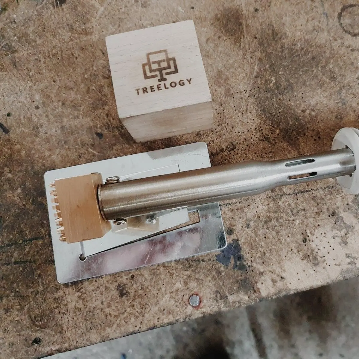 Brass branding iron with the Treelogy logo resting on a workbench next to a wooden block burned with the Treelogy logo and wordmark